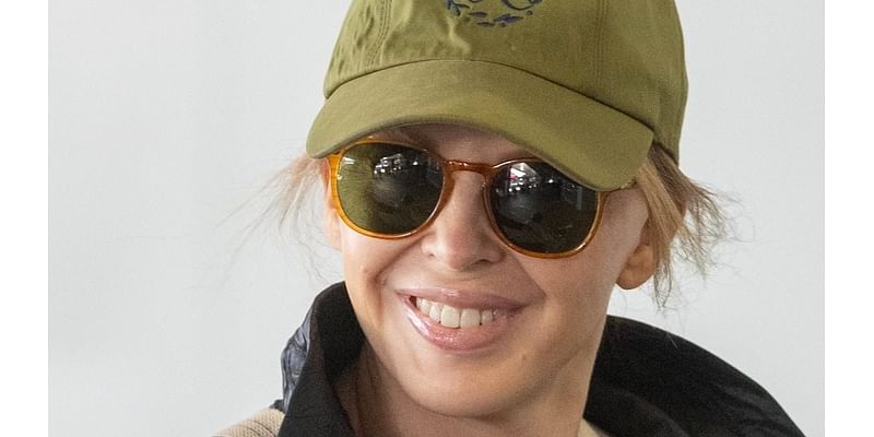 Kylie Minogue tries to go incognito under a large coat and hat while touching down in Sydney as pop star prepares to announce Grammy nominees