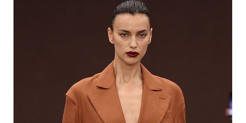 Irina Shayk goes braless beneath a longline tan coat while Amelia Gray Hamlin flashes her abs on the Ferrari runway during Milan Fashion Week